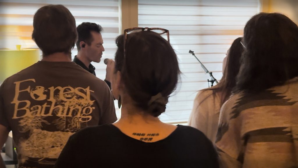Alan Robertson singing during an intimate live music gathering with audience members listening and participating.